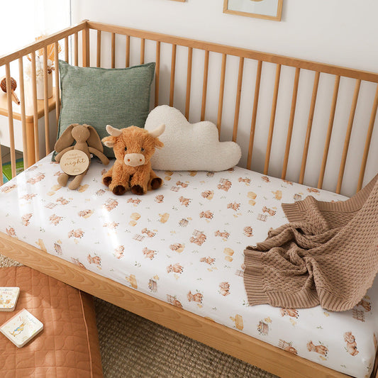 Snuggle Hunny Highland Cows organic fitted cot sheet on a cot
